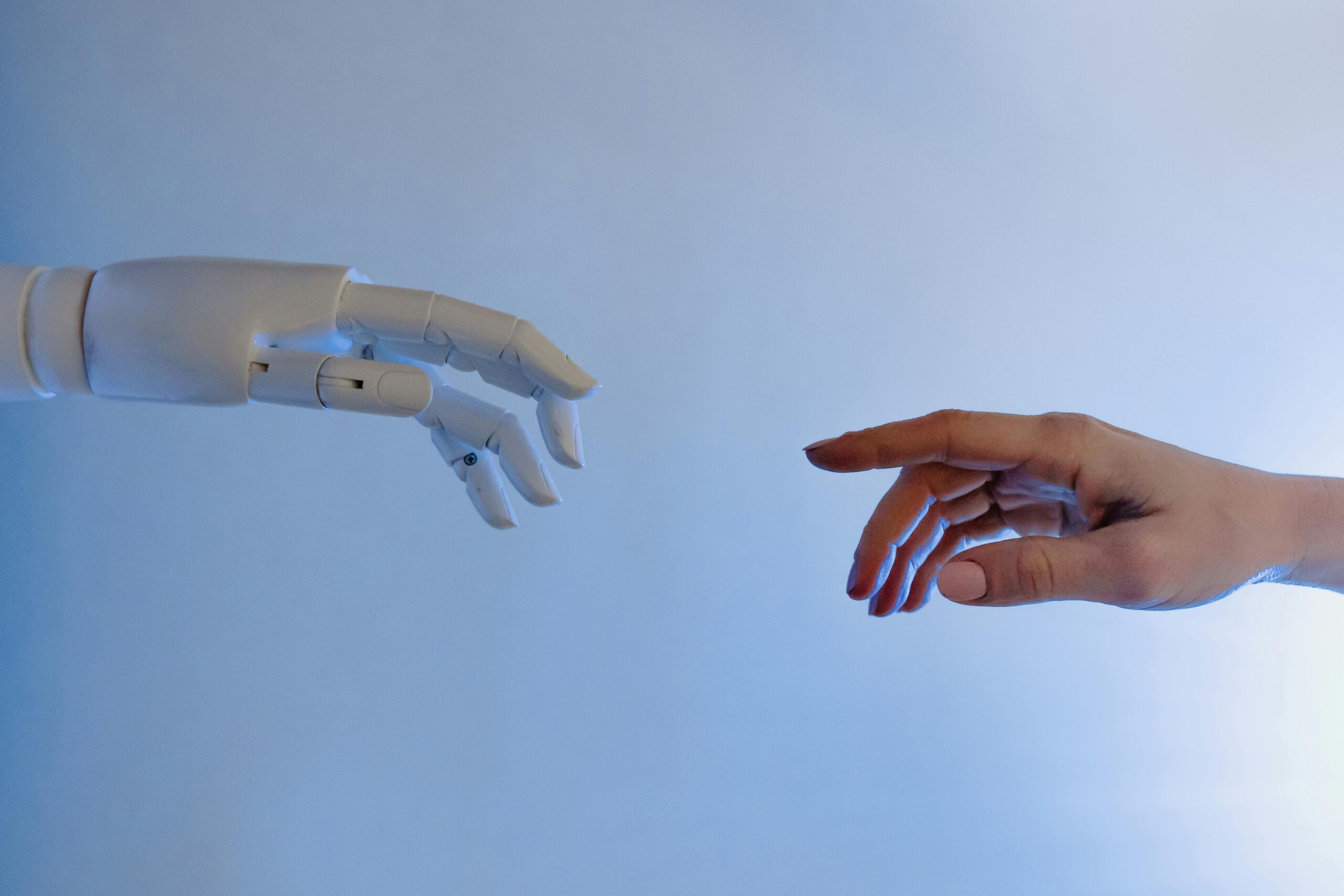 A robotic hand and a human hand reaching out to touch the other.