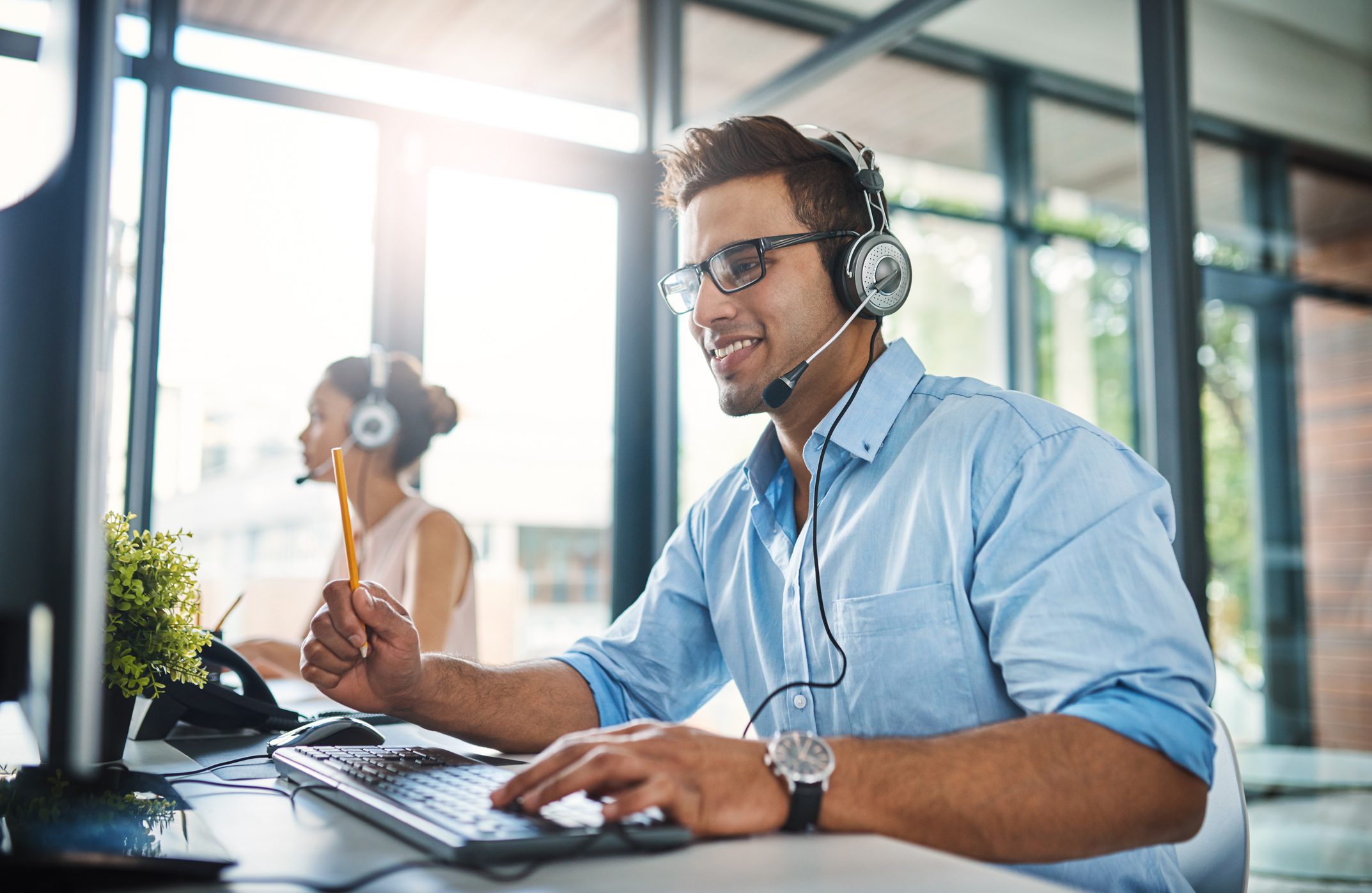 Cropped shot of a handsome young man working in a call center with a female colleague in the background