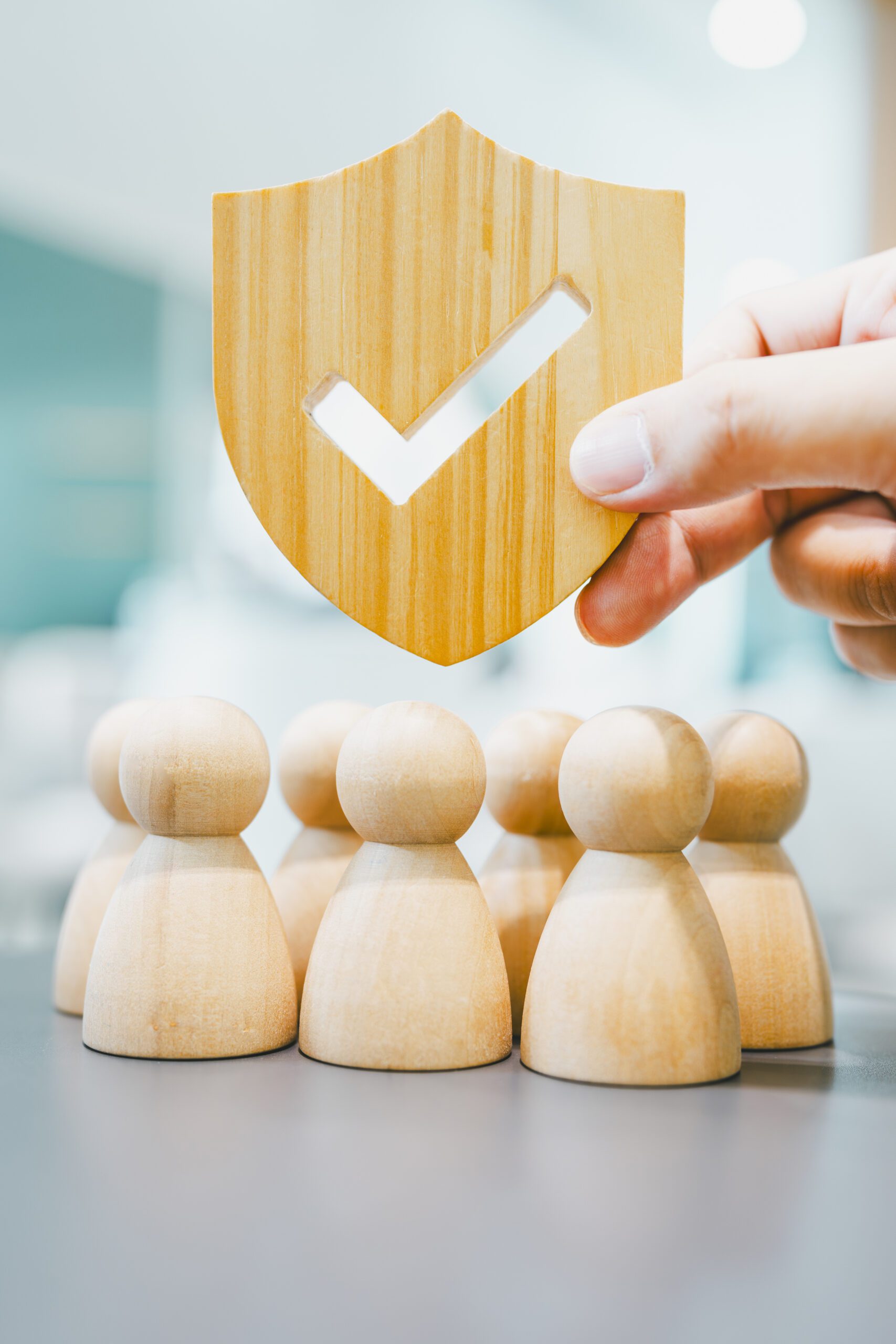 7 wooden figures under a wooden security shield held up by a hand.