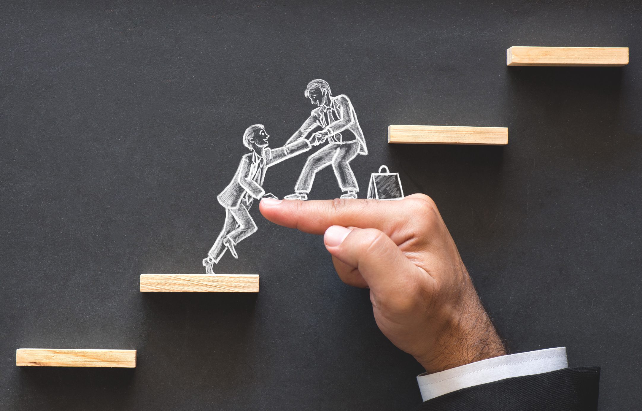 A chalkboard drawing of one businessman helping another up a set of stairs